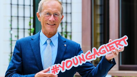 Staatsminister Wintermeyer hält den Schriftzug #youngagiert hoch und lächelt in die Kamera.