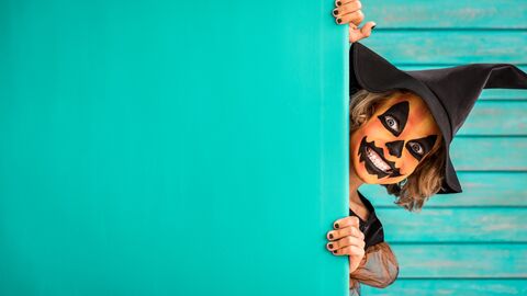 Kind in Hesenkostüm und schauriger Gesichtsbemalung guckt hinter einer Wand hervor und zieht eine Schreck-Grimasse