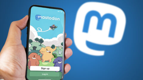 Die Hessische Landesregierung informiert über Ihre Arbeit bei Mastodon. Vor einem blauen Hintergrund hält eine Person ein Smartphone in der Hand. Auf dem Bildschirm ist die App Mastodon zu sehen.