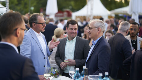 Der stellvertretende Ministerpräsident, Tarek Al-Wazir, inmitten der Gäste auf dem Hessenfest in Berlin, an einem Stehtisch stehend im Gespräch mit zwei Gästen