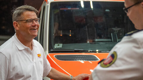 Ministerpräsident Rhein vor einem Einsatzfahrzeug im Gespräch mit einer weiteren Person.