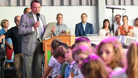 Kultusminister Lorz mit Mikrofon in der Hand an einem Podium, im Vordergrund viele Kinder