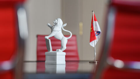 Ein Tisch mit einer kleinen Löwen-Statue, daneben eine kleine Hessen-Flagge. Vor und hinter dem Tisch stehen rote Konferenzstühle.