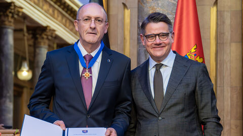 Zwei Personen stehen nebeneinander und halten die Auszeichnung hoch.