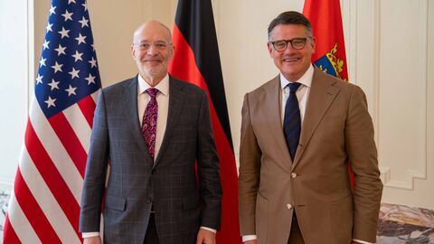 Empfang Alan Meltzer Zwei Männer stehen vor Flaggen der USA, Deutschland und Hessen.