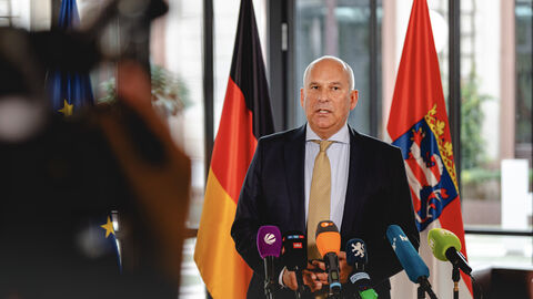 Innen- und Heimatschutzminister Roman Poseck im Interview vor dem Rüstungsgipfel. Innen- und Heimatschutzminister Roman Poseck Wirtschaftsminister Mansoori steht vor Mikrofonen in einer Interviewsituation.