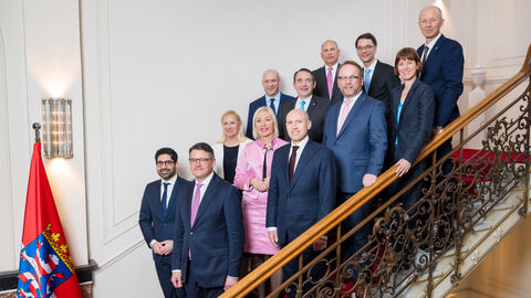 Offizielles Portraitfoto des neuen Hessischen Kabinetts. Sie stehen alle gemeinsam auf einer Treppe und lächeln in die Kamera.