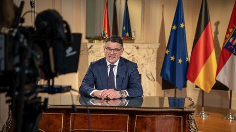 Mann sitzt an Schreibtisch, Kamera ist auf ihn gerichtet. 