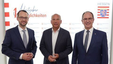 Drei Männer im Anzügen blicken in Kamera. Im Hintergrund sieht man das Hessen-Logo