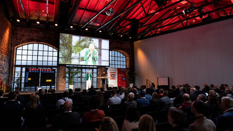 Frau steht auf Bühne und spricht zu Publikum.