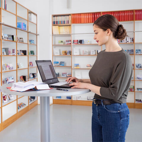 Arbeitgeber Land Hessen Eine junge Frau steht an einem Stehtisch und arbeitet.